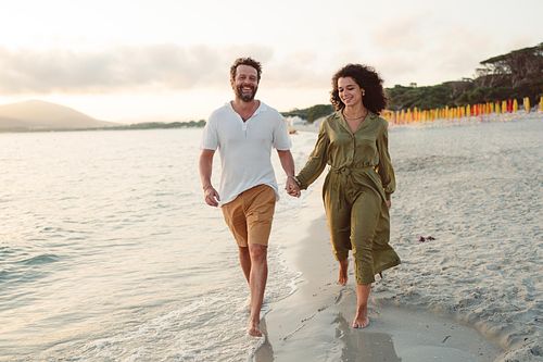 "coppia passeggia tenendosi per mano in spiaggia ad Alghero"