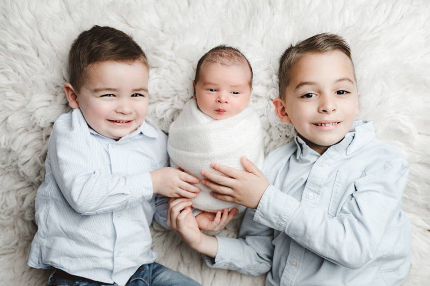 Newborn baby comfortably nestled in between siblings, styled by Houston newborn photographer Amanda Mandola.