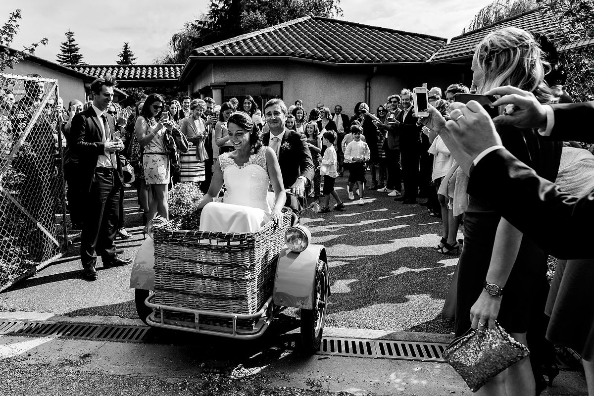Tarif Photographe Mariage - Sebastien CLAVEL Photographe - Arriv&eacute;e joyeuse de la mari&eacute;e en triporteur d&eacute;cor&eacute;, accueillie par les invit&eacute;s applaudissant sous le soleil