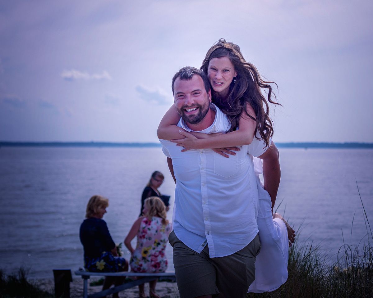After the wedding ceremony the groom is carrying his bride on the back across the sand in assateague Island