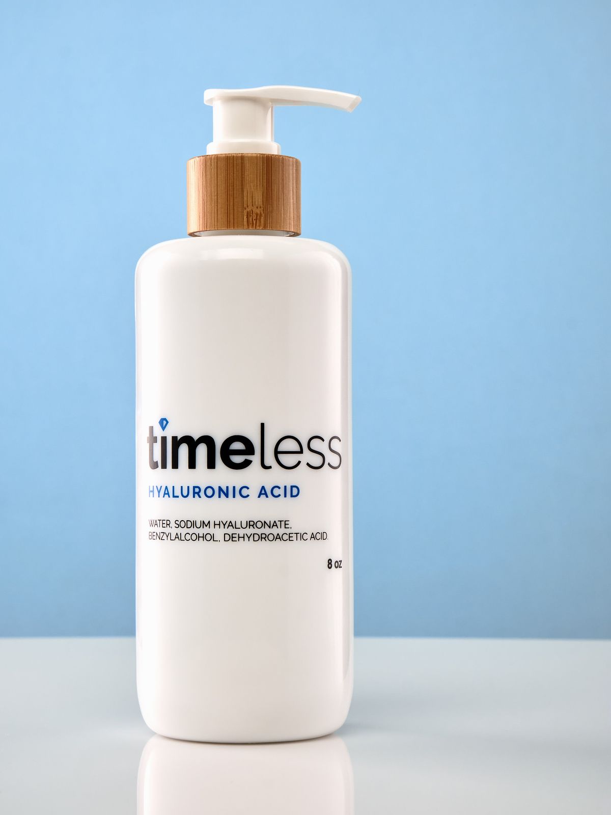 White cosmetics pump bottle on a reflective white base and blue backdrop.