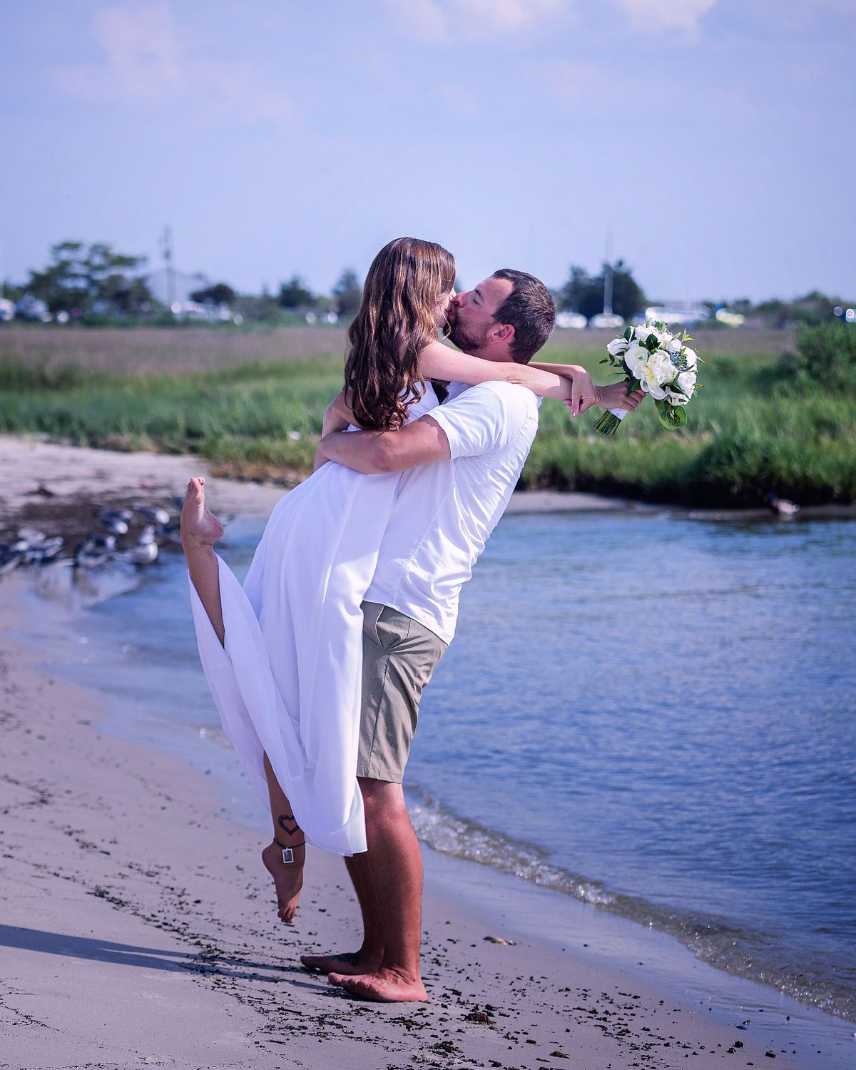 Groom lifting up the bride on the beach in dewey beach, with the bride kicking on of her legs back and kissing the groom