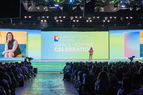 Brenda Darden Wilkerson speaks on the main stage at the 2024 Grace Hopper Celebration in Philadelphia, with a full audience and event branding lit behind her.