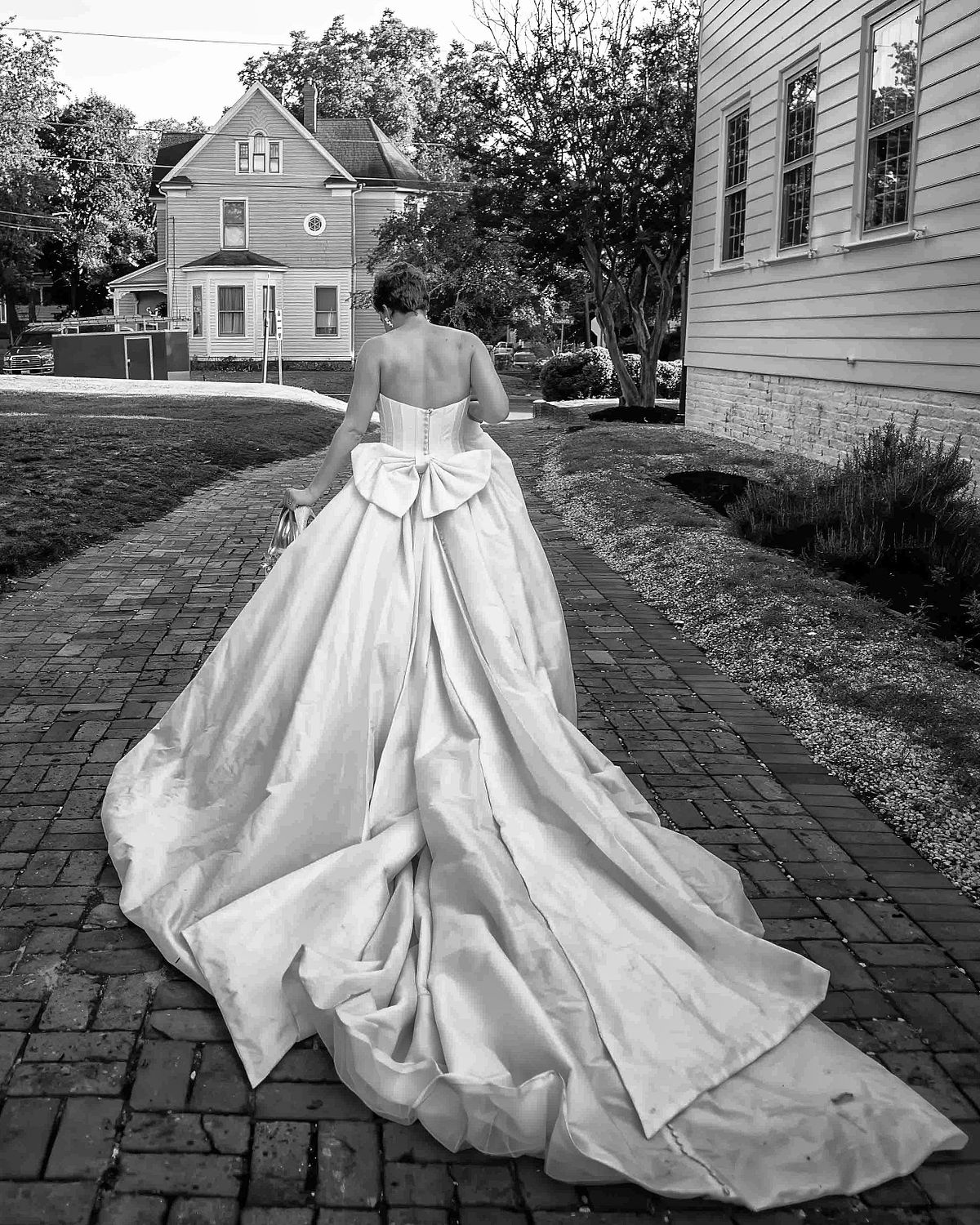 a bride, in a ballgown dress, with long train, and a big bow, walking away, deep in thought in this black and white fine art photo