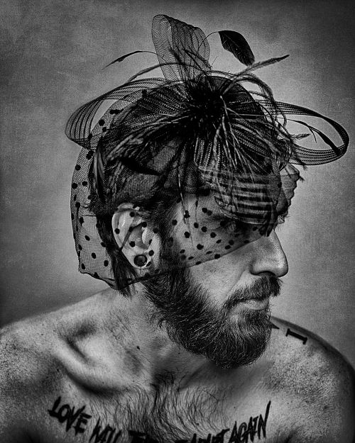 Portrait en noir et blanc d&rsquo;un homme barbu et tatou&eacute; portant une voilette d&eacute;licate, exprimant la tendresse masculine assum&eacute;e et la libert&eacute; d&rsquo;identit&eacute; &mdash; photographie fine art par Pascal Yennis, Namur, Belgique.