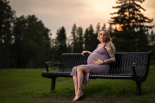 Expecting mother sitting on a bench in the park during sunset.