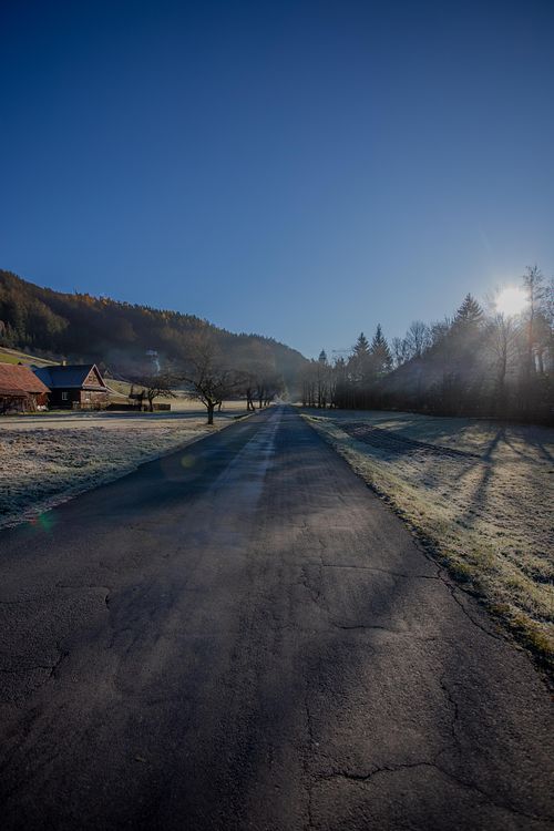 Route sombre avec lueur au loin, paysage dépouillé.