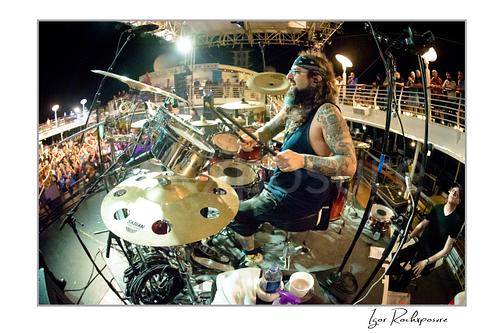 Mike Portnoy Live Concert Print  Horizontal color image of Mike Portnoy playing drums on stage at night in a wide fisheye concert scene with the crowd and ship deck behind him