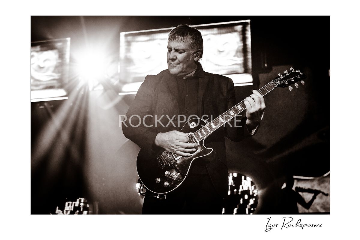 Horizontal concert photography of Alex Lifeson playing electric guitar in black and white photography under stage lighting