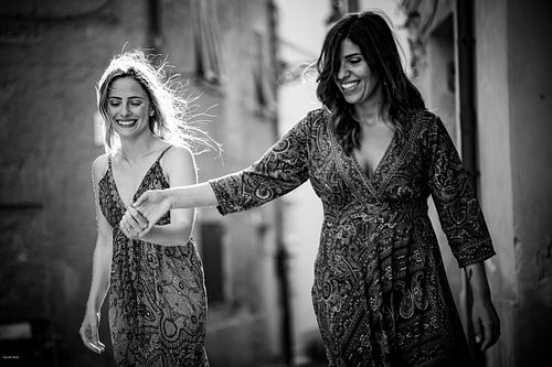 "coppia passeggia mano nella mano sorridente per le strade di Alghero"