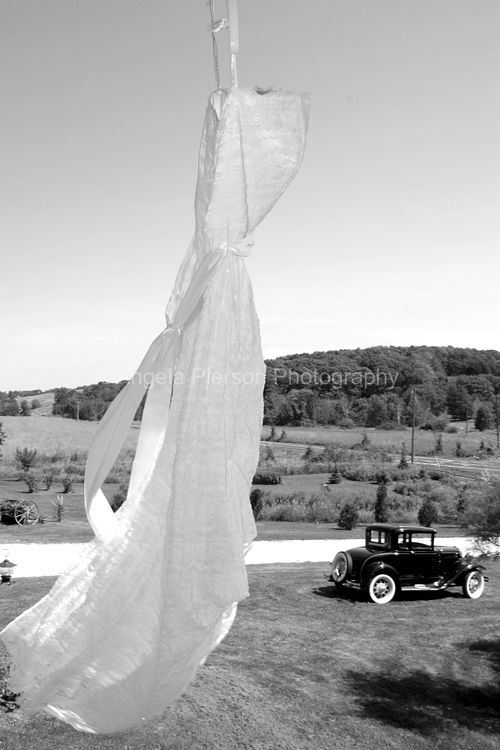 A black and white image of a wedding dress blowing in the wind and a vintage car in the background