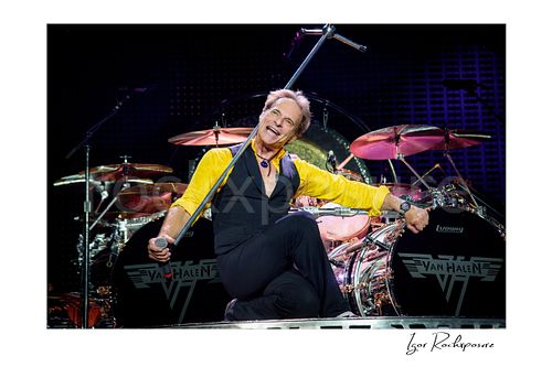Horizontal color image of David Lee Roth of Van Halen posing on stage in front of Alex Van Halen’s drum kit