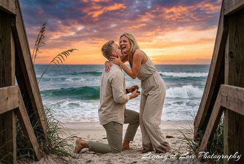 Man kneeling for a spontaneous sunset beach proposal in Jacksonville, framed by wooden stairs by Legacy of Love Photography.