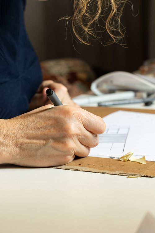 Närbild av hand som ritar med penna på papper vid bord – fokus på kreativ process.