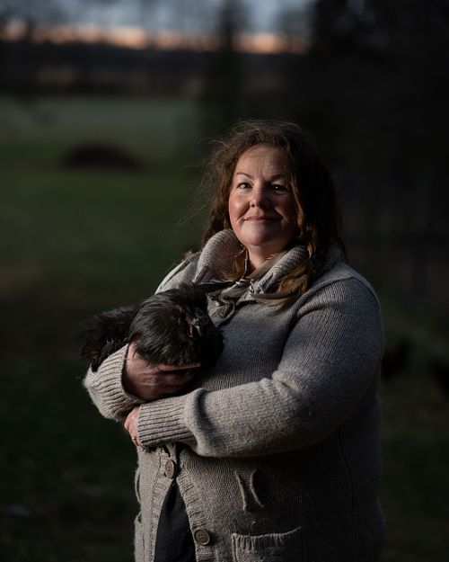 A woman proudly holds her chicken on her farm.
