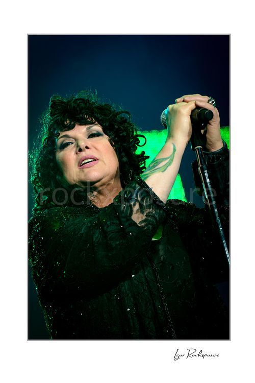 Vertical color image of Ann Wilson singing into a microphone during a Heart concert in a close-up portrait under vivid green stage light