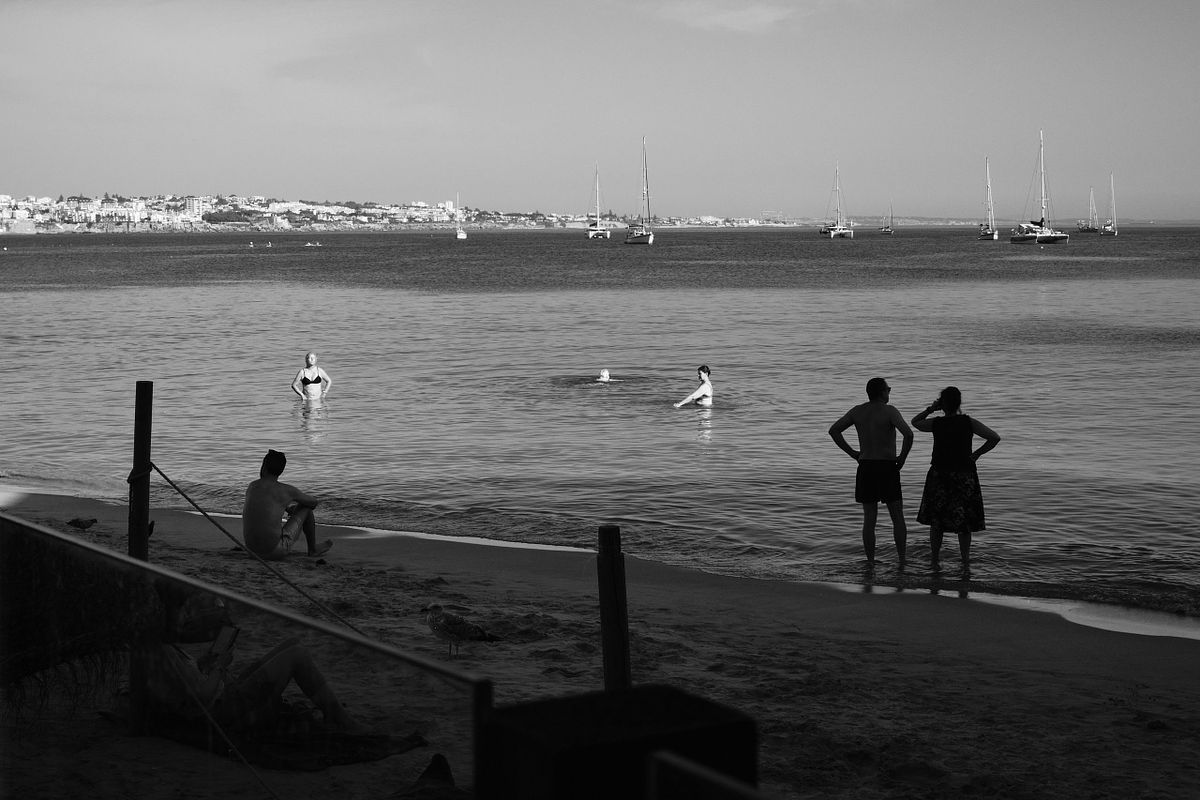 People enjoying a tranquil day at the beach in Portugal with boats in the background, captured by photographer Sandeep Gajula